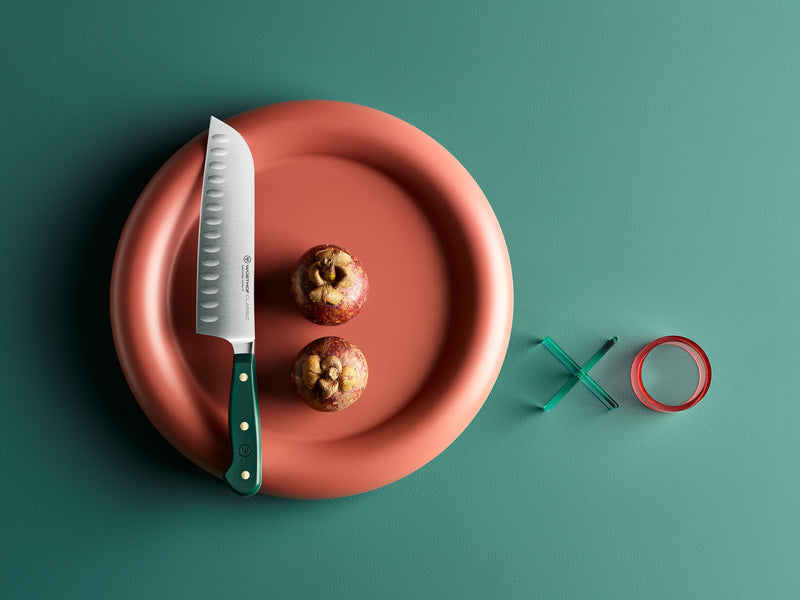 Knife on a red plate with two apples, next to green and red rings on a teal background