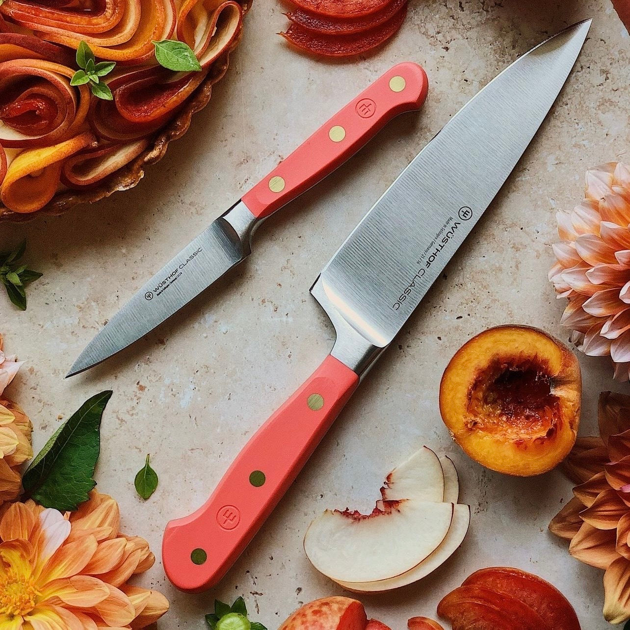 Two knives with red handles on a surface with fruit and flowers