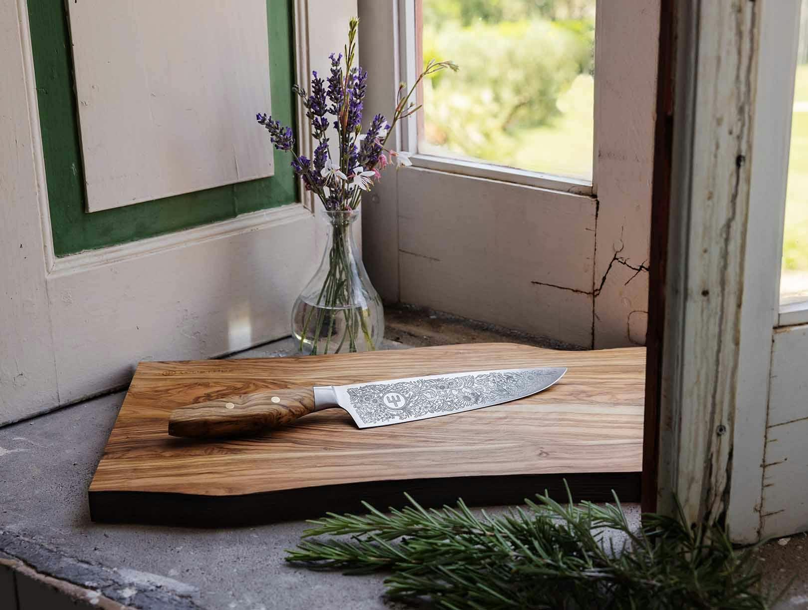 Amici 1814 Chef's knife in front of window on the dune cutting board