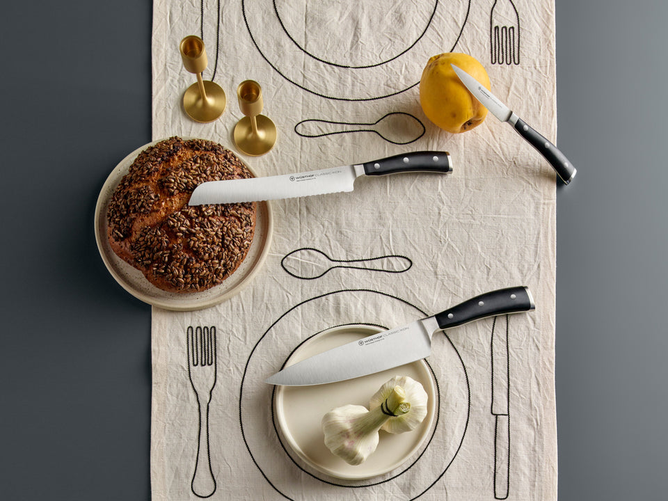 Table setting with bread, knife, and lemon on a decorative tablecloth.