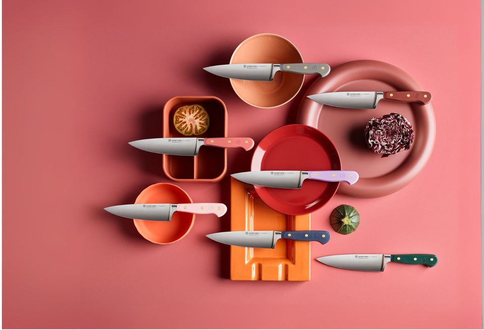 Set of knives on colorful plates against a pink background