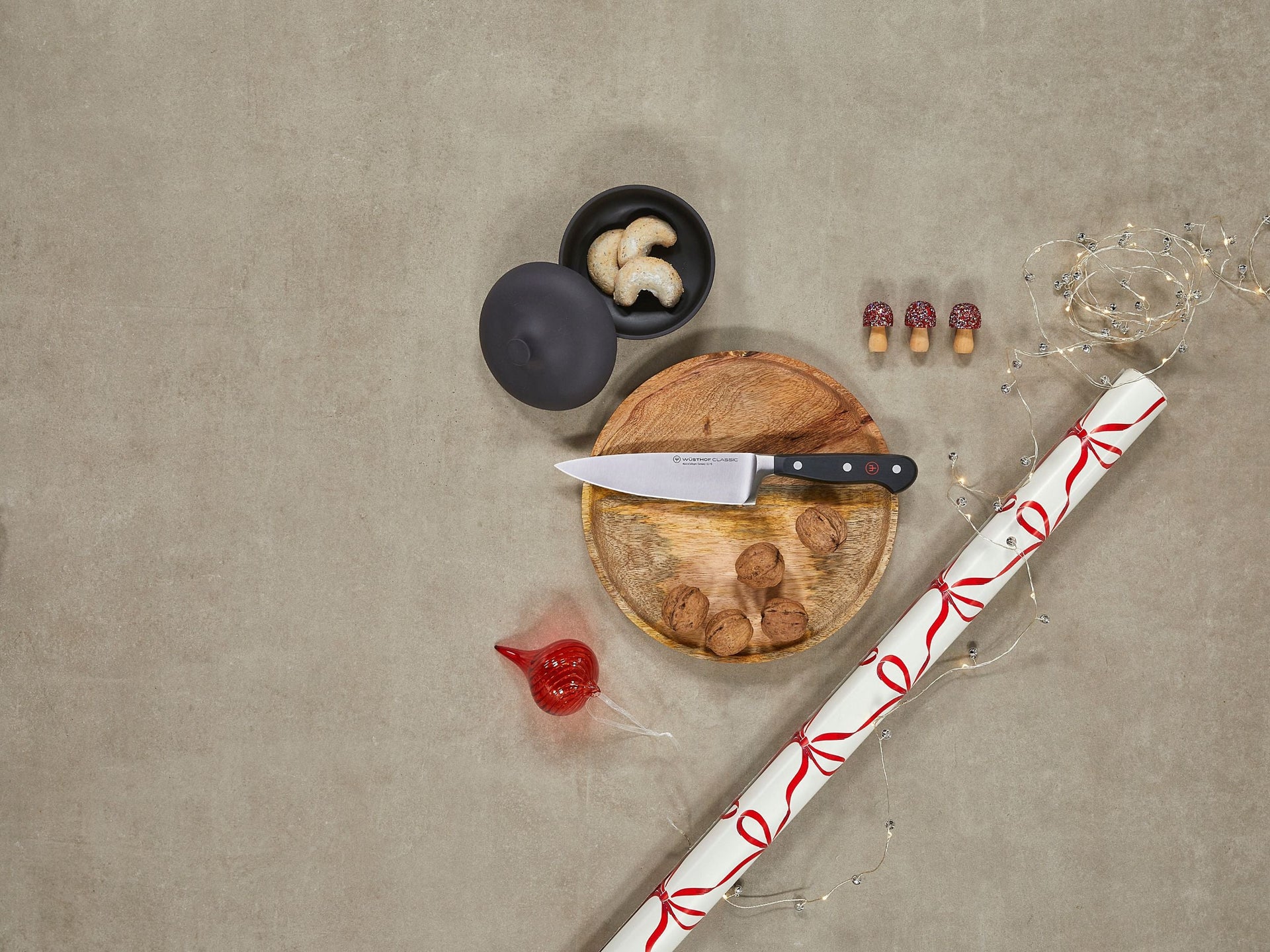 Knife on a wooden cutting board with mushrooms, a bottle cap, and a wrapped gift on a concrete surface.