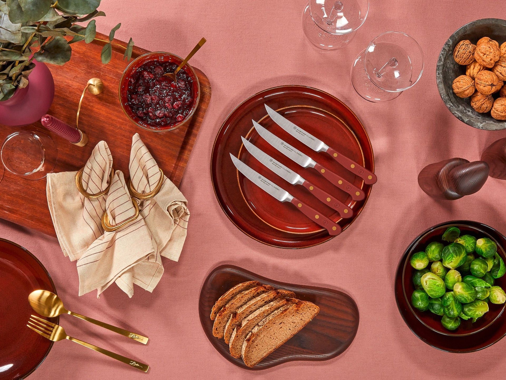 Dinner table setting with bread, brussels sprouts, and cutlery on a pink surface.