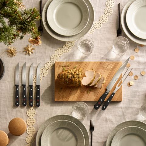 Dining table setting with plates, cutlery, and a wooden cutting board with sliced bread.